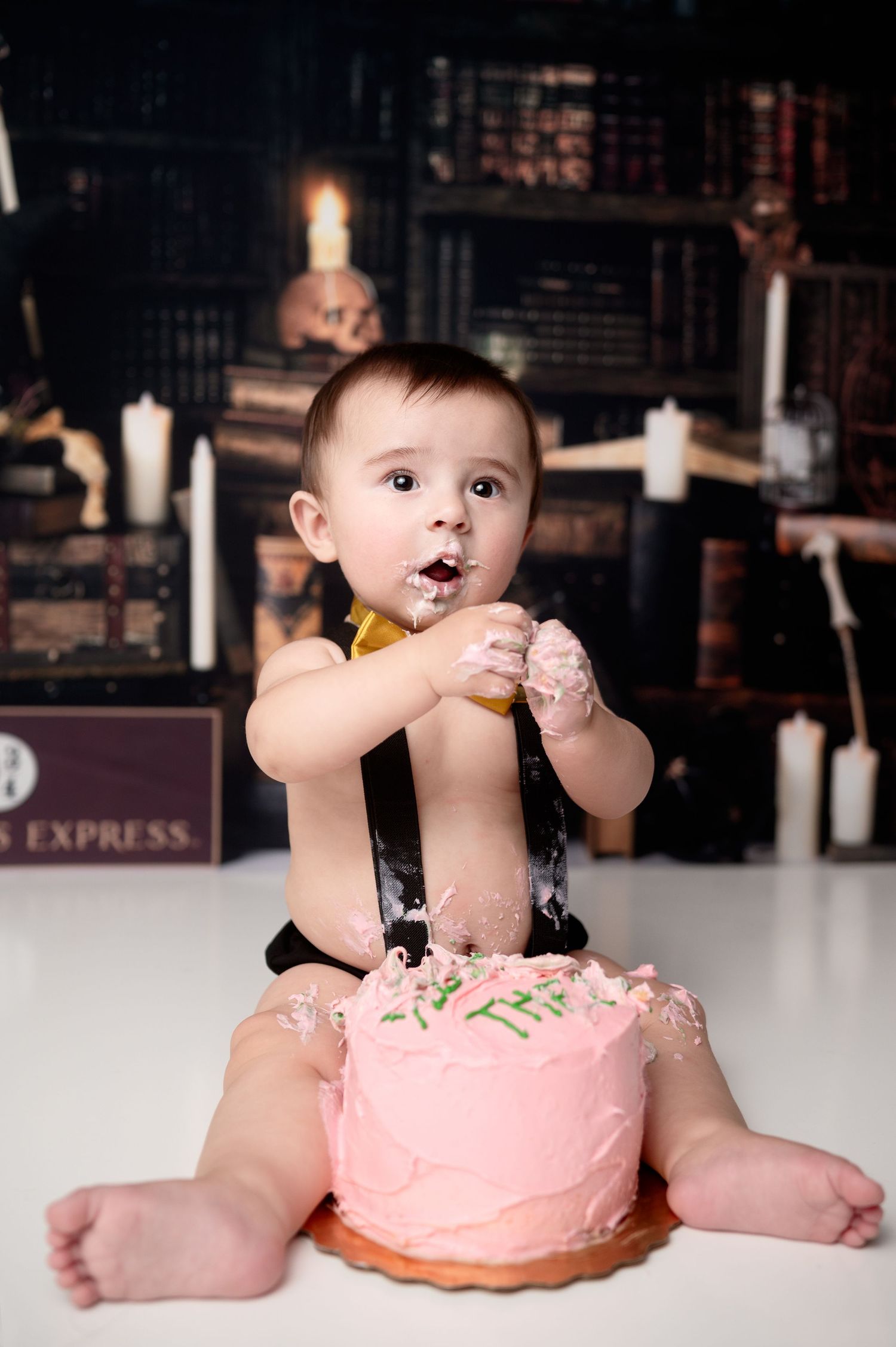 Baby getting messy with pink birthday cake during cake smash photoshoot.