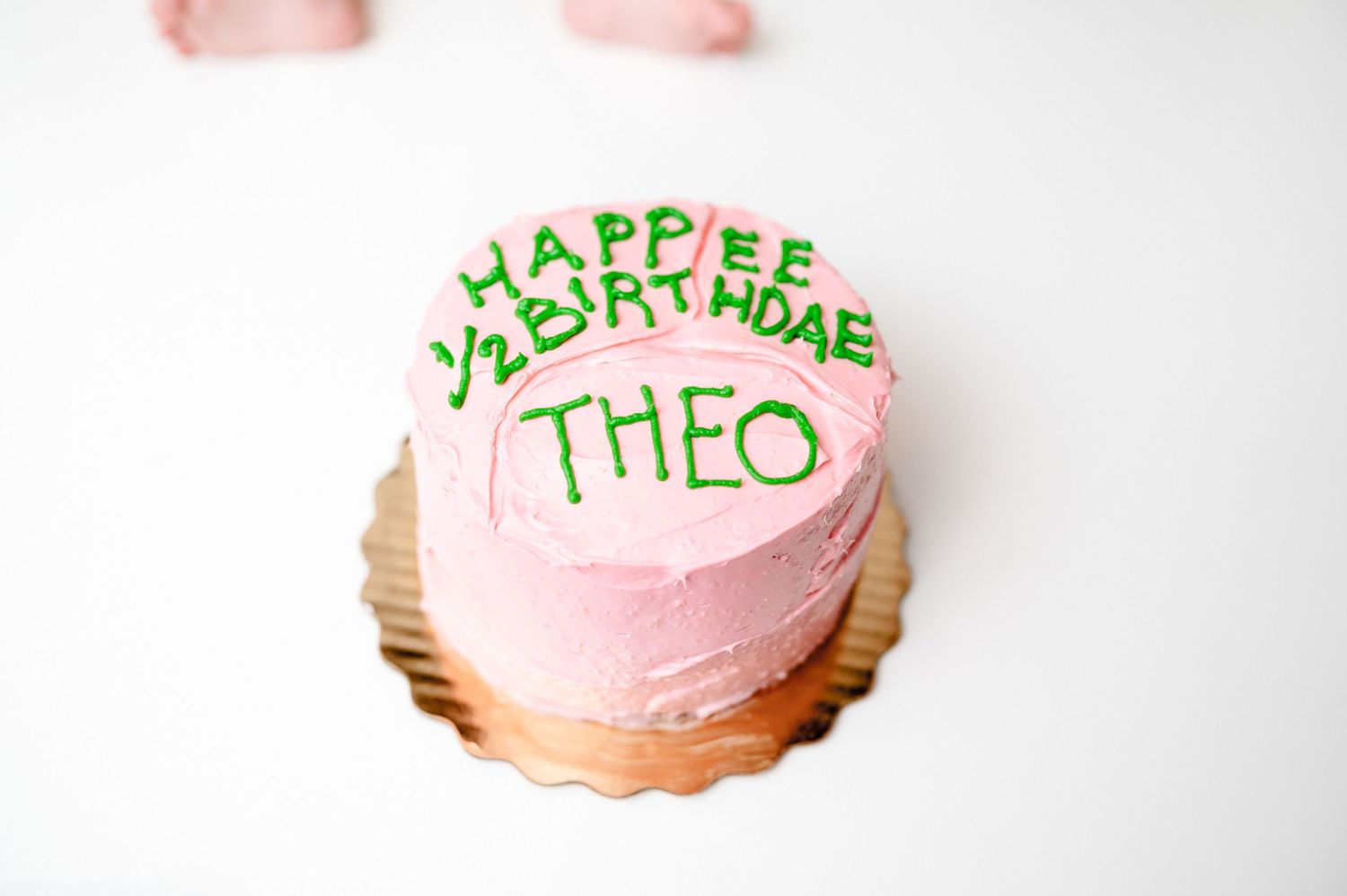 Pink birthday cake with green lettering spelling Happy Valentine Theo.