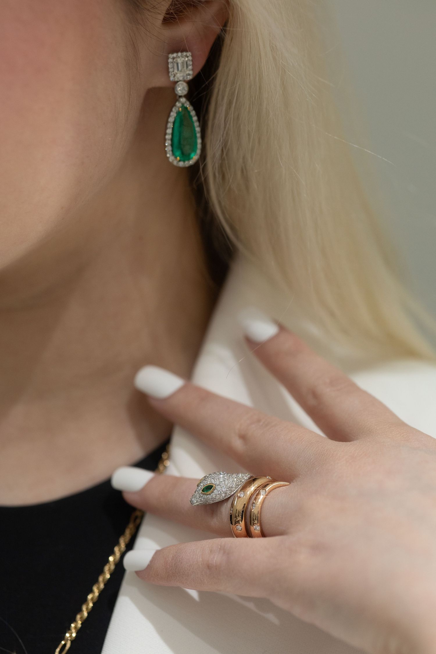 Emerald drop earring and stacked rings with white manicure in elegant jewelry styling.