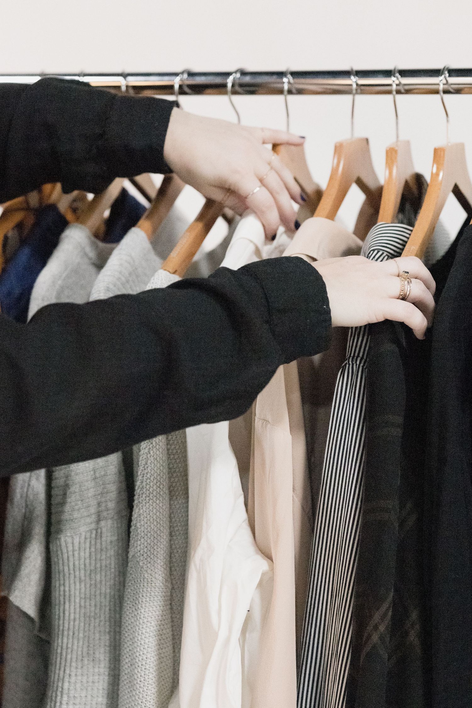 Hands browsing through clothing on wooden hangers displaying various gray and neutral colored garments.