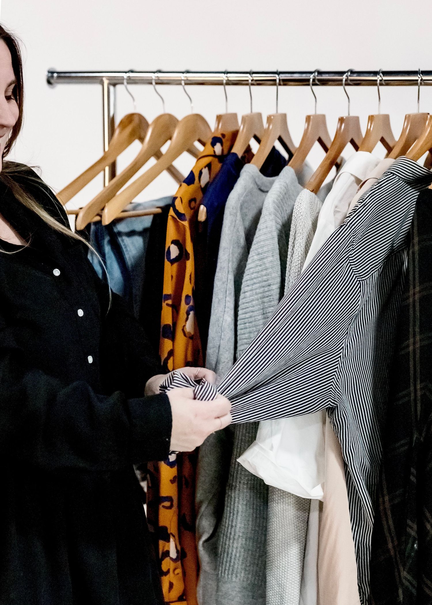 Clothing rack featuring a curated collection of neutral and striped garments on wooden hangers.