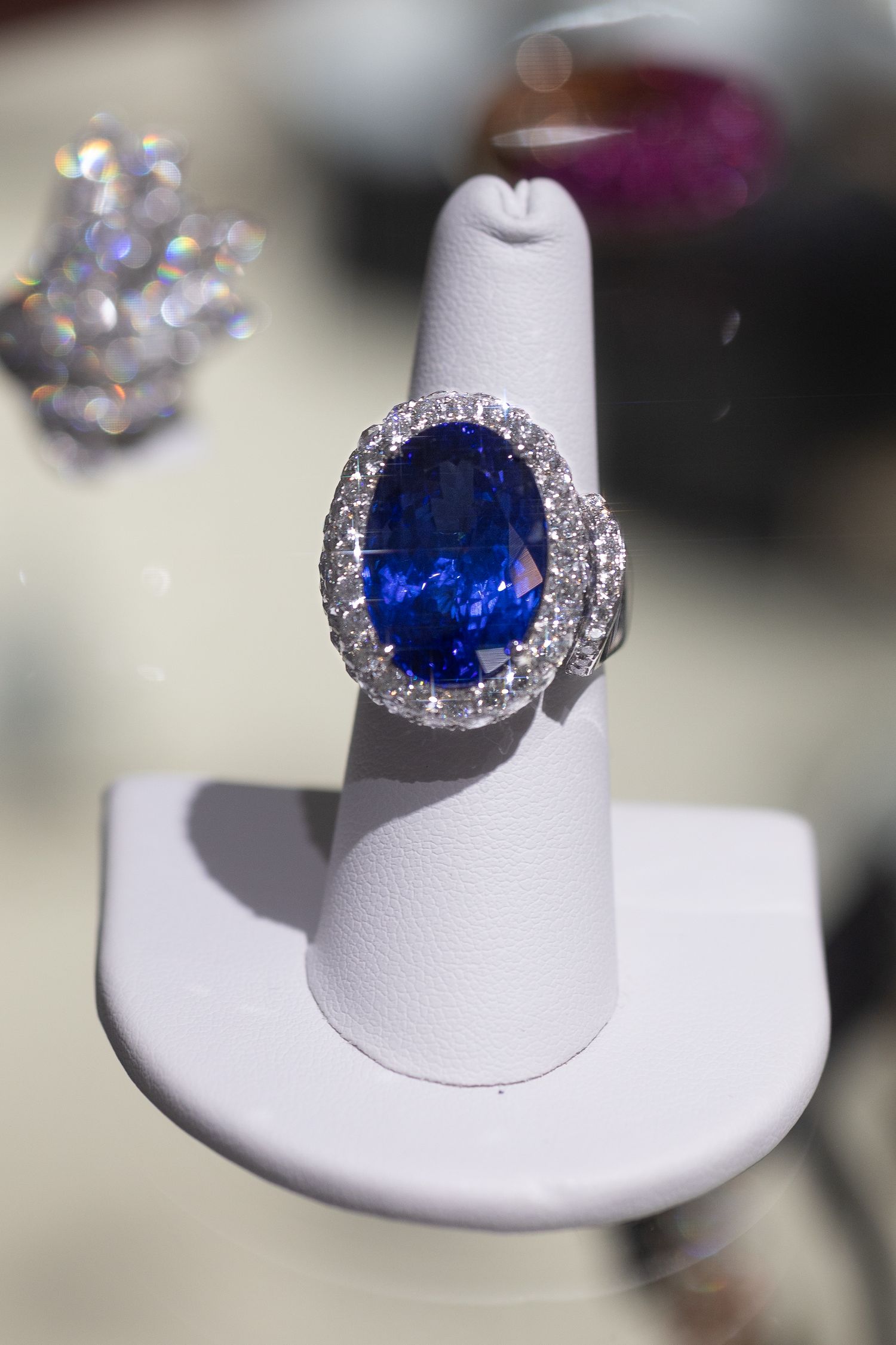 Stunning sapphire and diamond halo ring displayed on white jewelry stand.