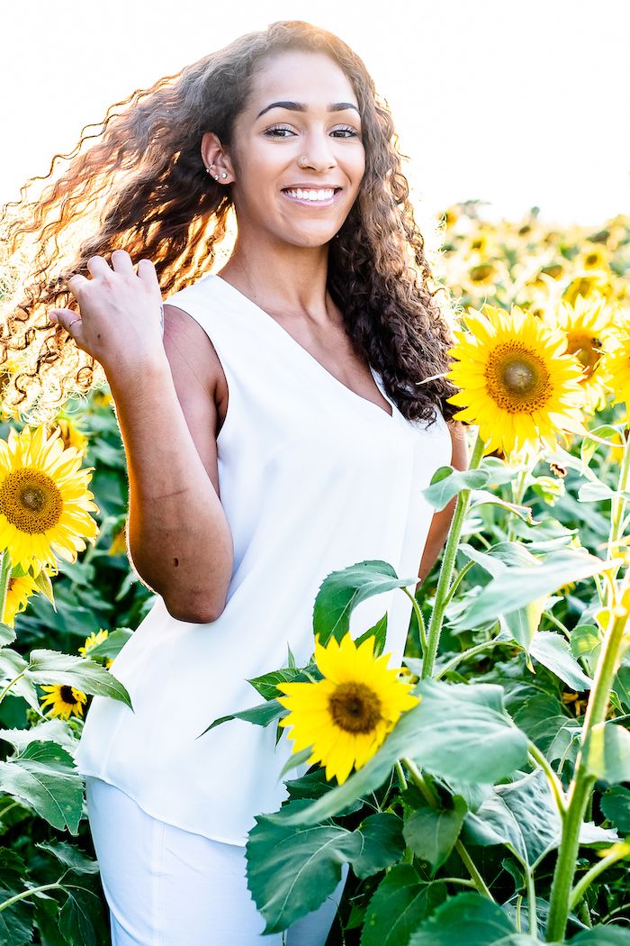 Portrait in white dress amid blooming sunflower field on sunny day.