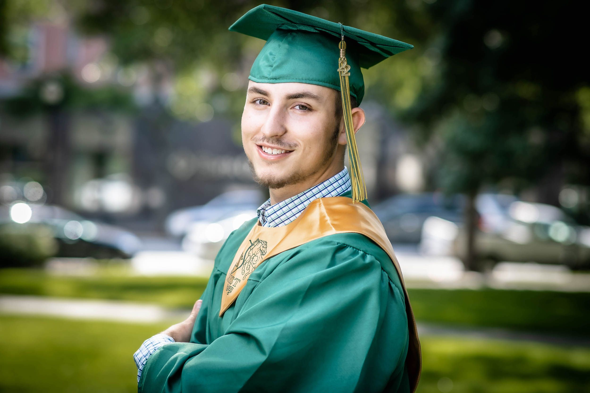Graduate in green cap and gown with gold tassel outdoors.
