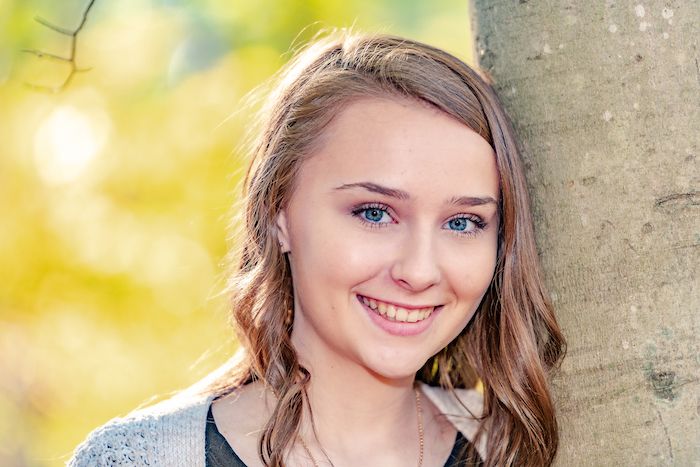 Portrait against autumn backdrop with soft bokeh lighting effects.
