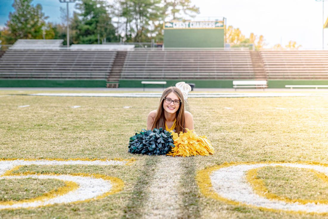 Cheerleader with pom poms posing on a football field during golden hour.