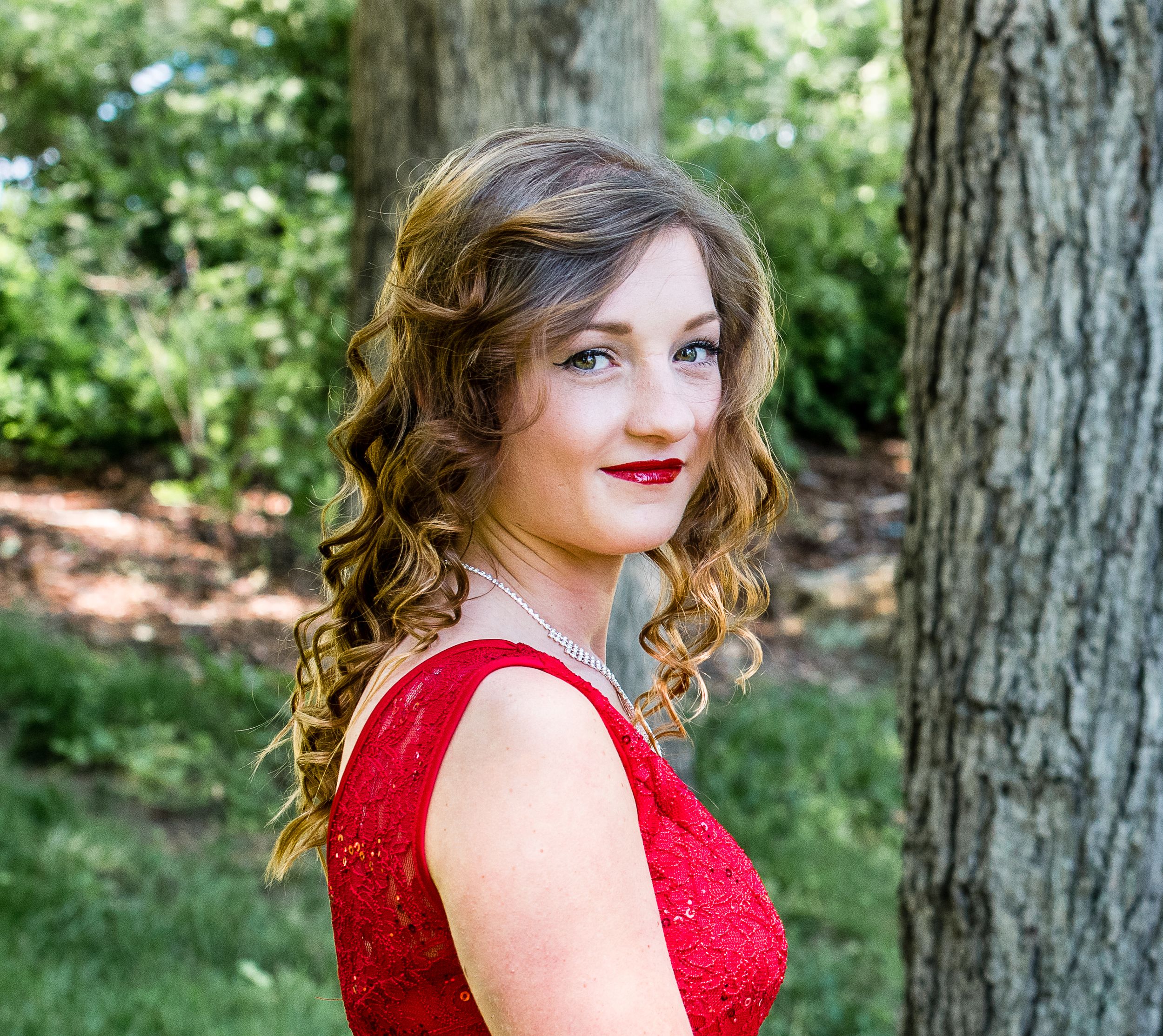 Portrait of woman in red formal dress against natural outdoor background.
