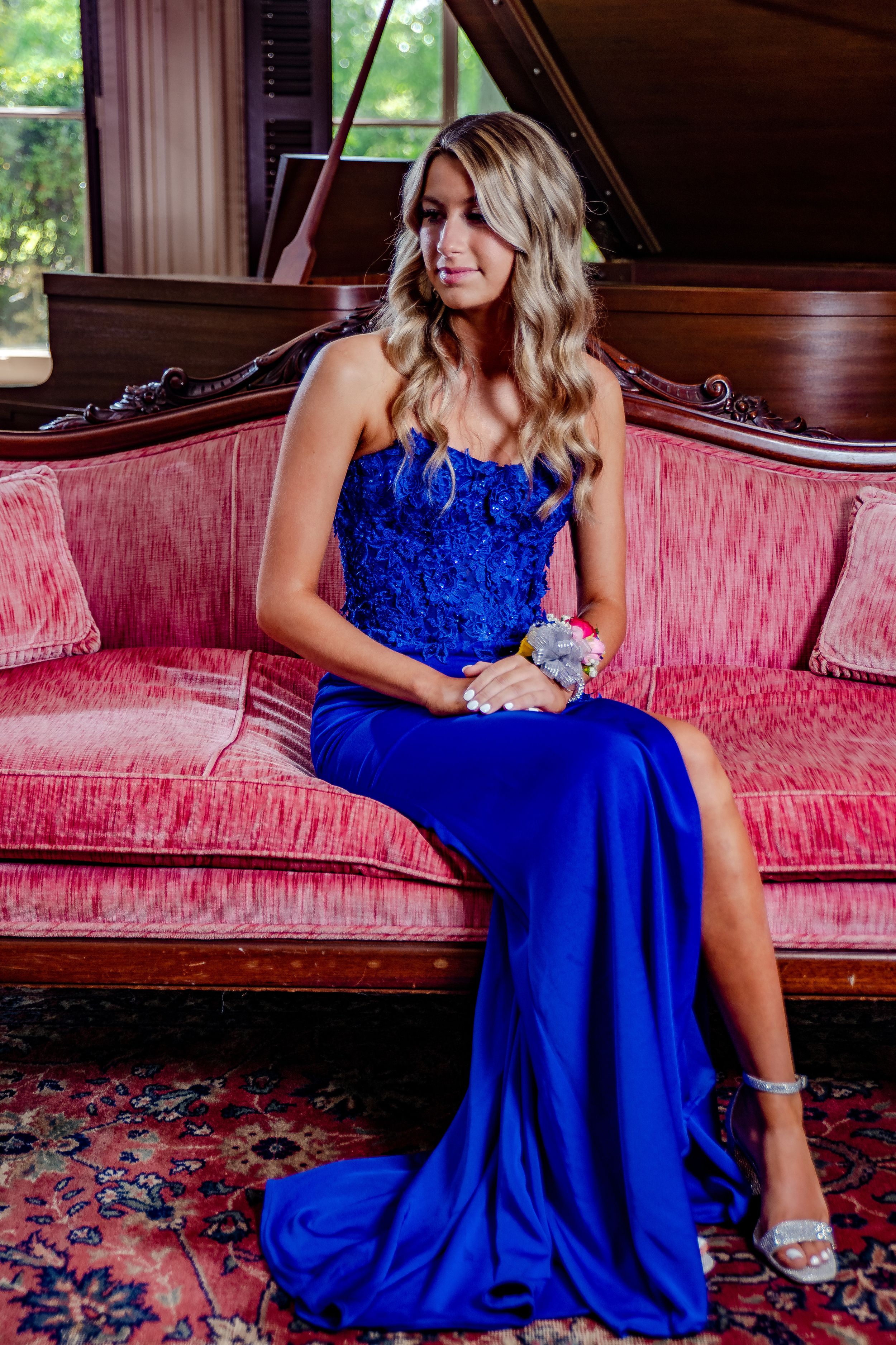 Woman in sparkly royal blue evening gown poses elegantly on vintage pink velvet sofa.