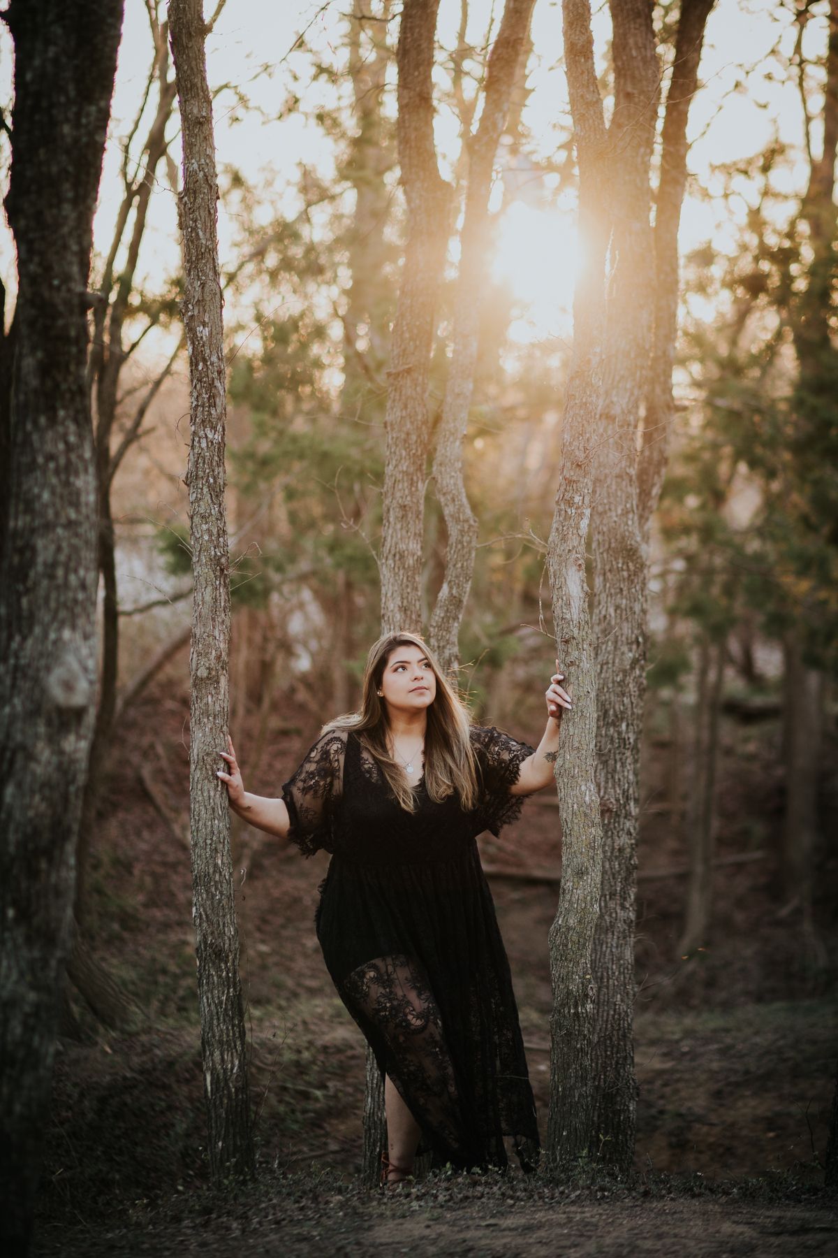 college senior girl standing between trees in black lace dress looking to the right