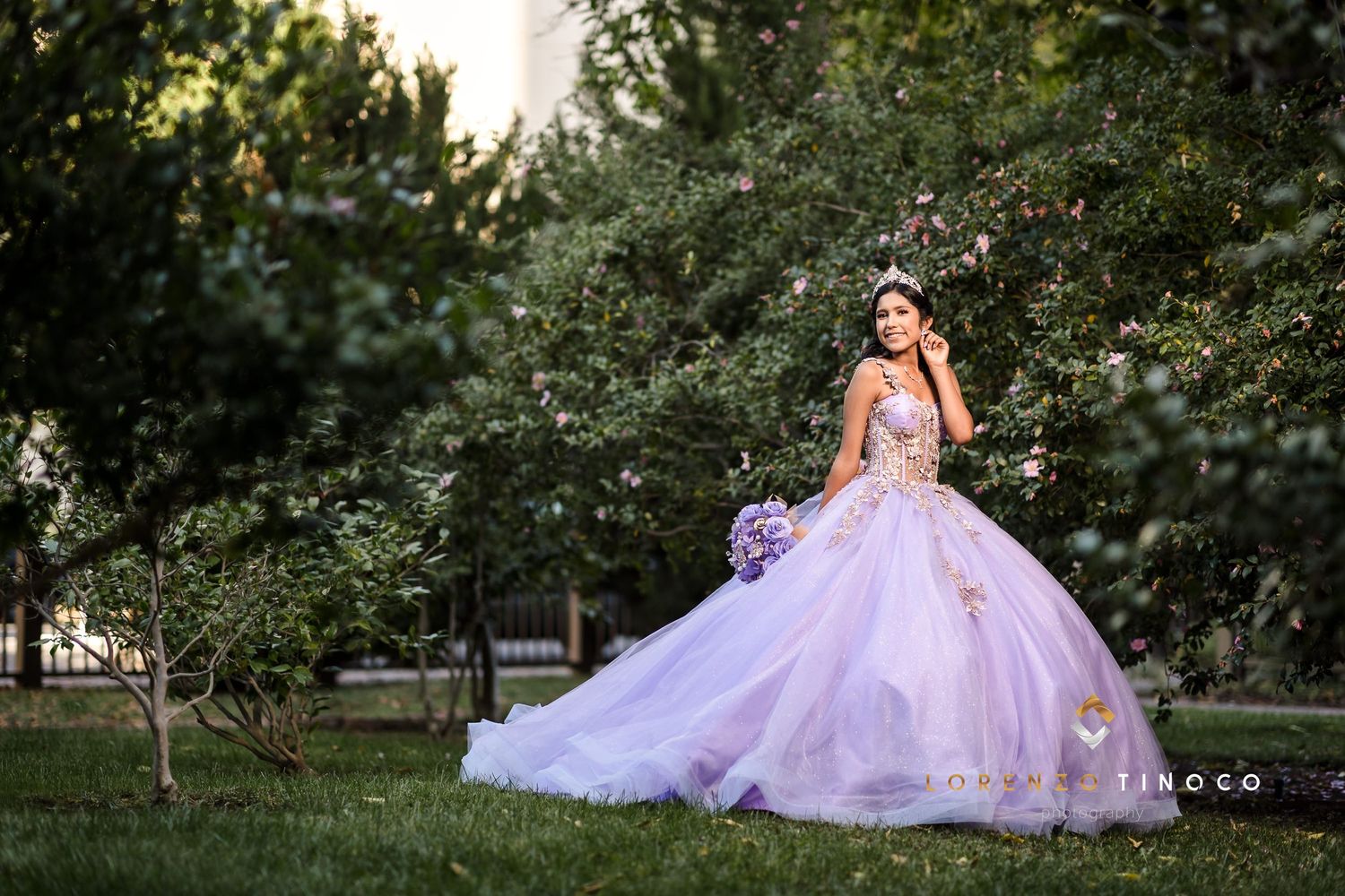 A lavender tulle ball gown glows in afternoon sunlight amidst lush garden greenery.
