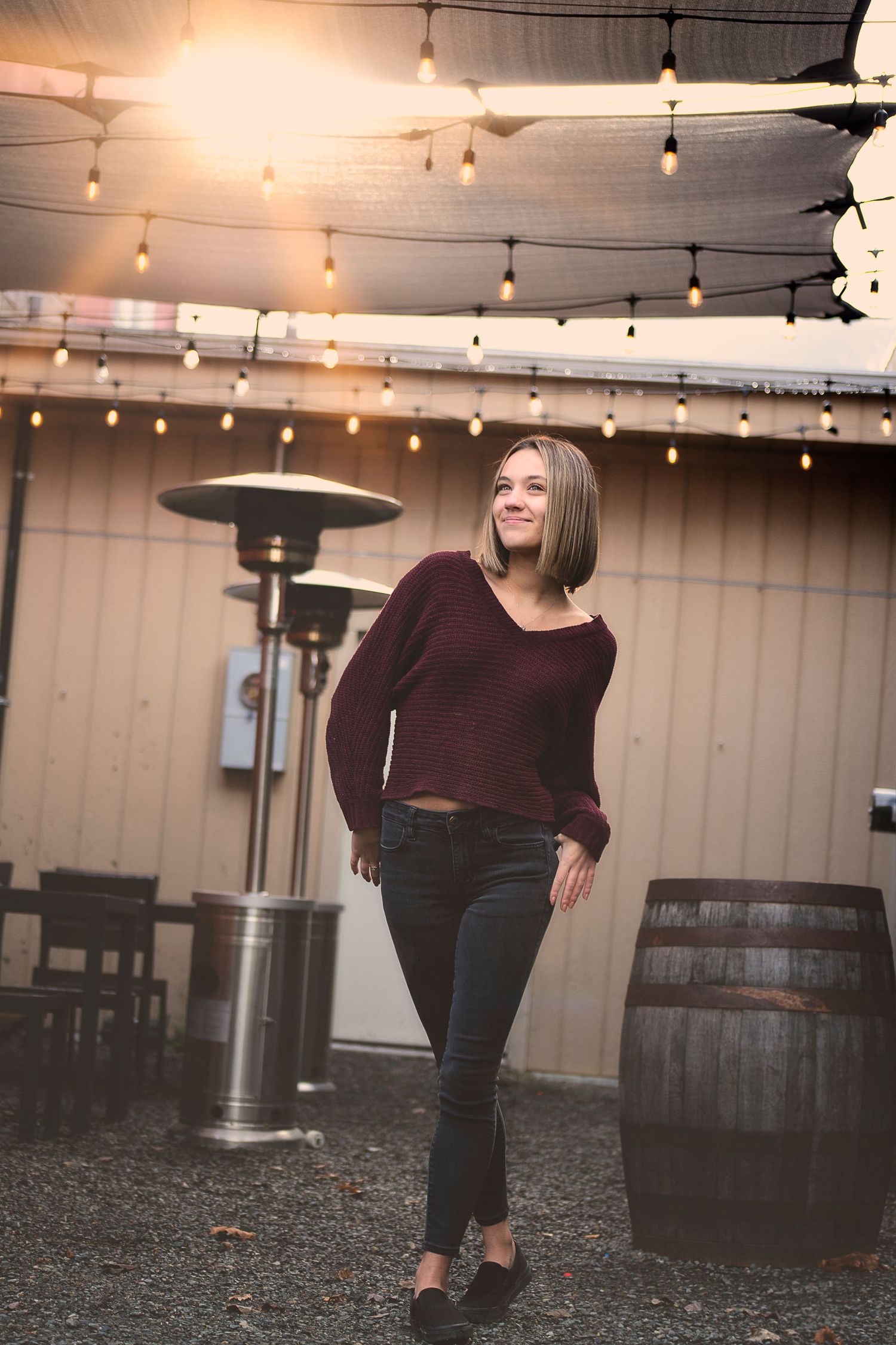 Person in burgundy top posing under string lights in outdoor setting.