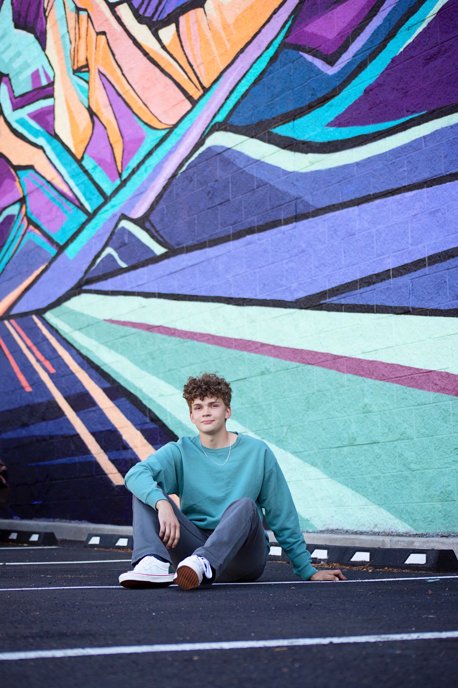 Person in teal sweater poses against vibrant geometric street art mural.