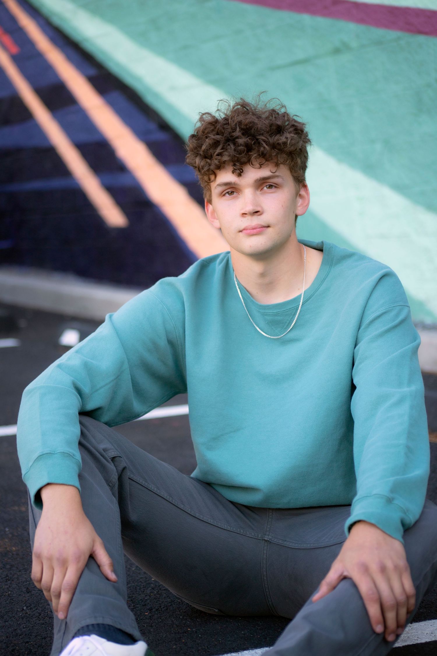 Young person in teal sweatshirt sits casually against colorful geometric wall art.