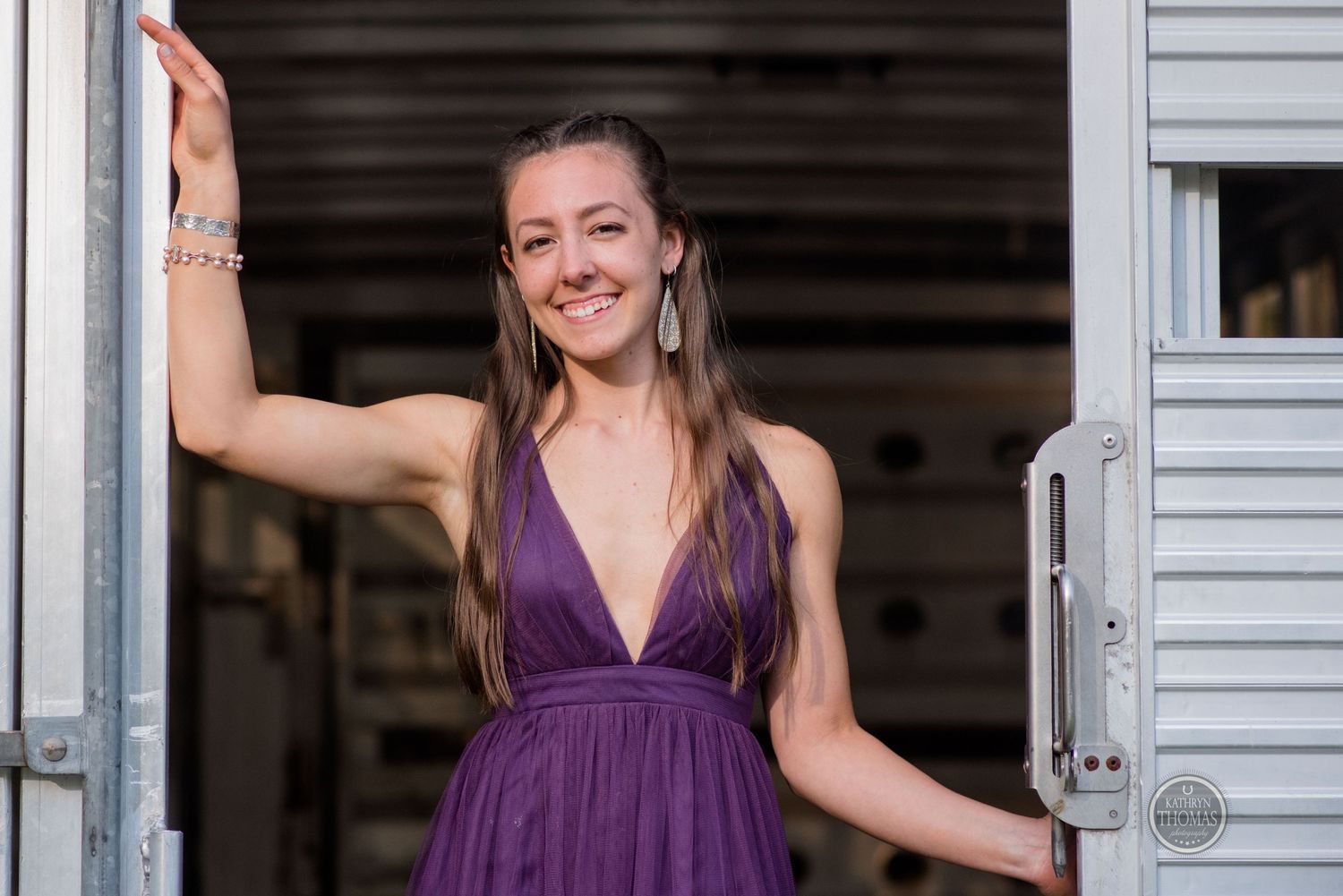 Someone smiles while posing in a deep purple formal dress in a trailer doorway.