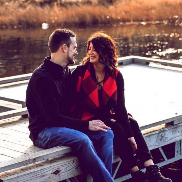 Couple sharing intimate moment on dock during sunset wearing casual attire.