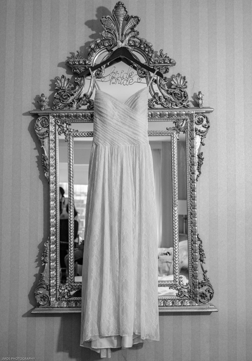 Elegant white wedding dress hanging on ornate vintage mirror.