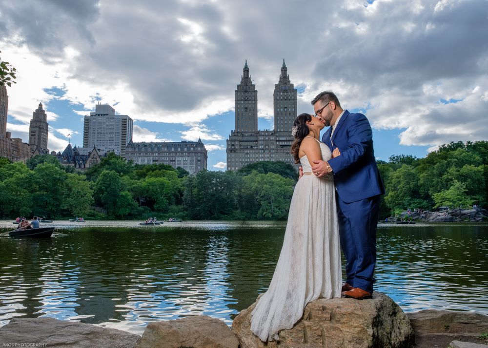 Romantic wedding portrait by Central Park lake with city skyline.