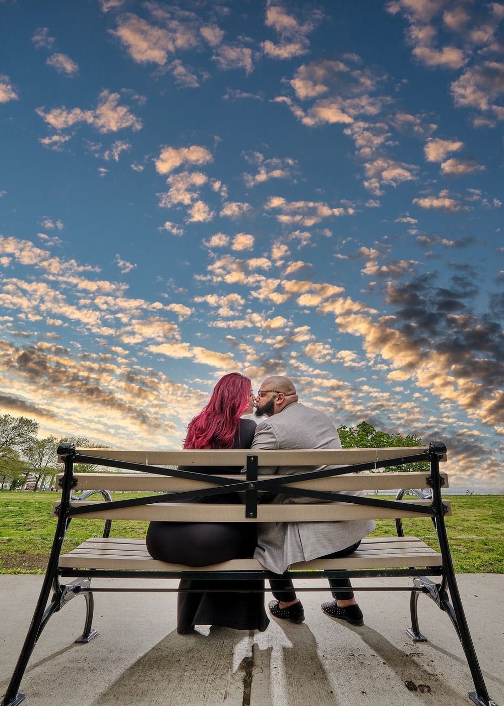 Silhouetted couple on bench against dramatic orange and blue cloudy sunset sky.