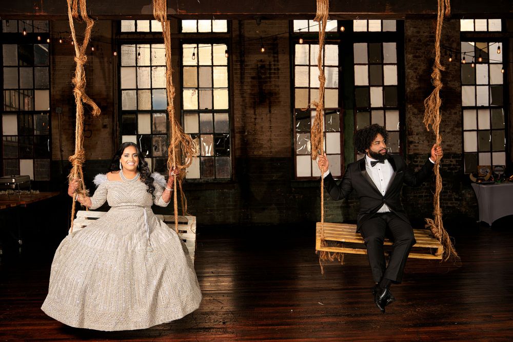 Wedding couple on rustic indoor swings in formal attire against industrial windows.
