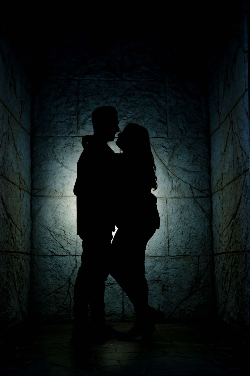 Dramatic silhouette of couple in backlit stone corridor with moody atmosphere.