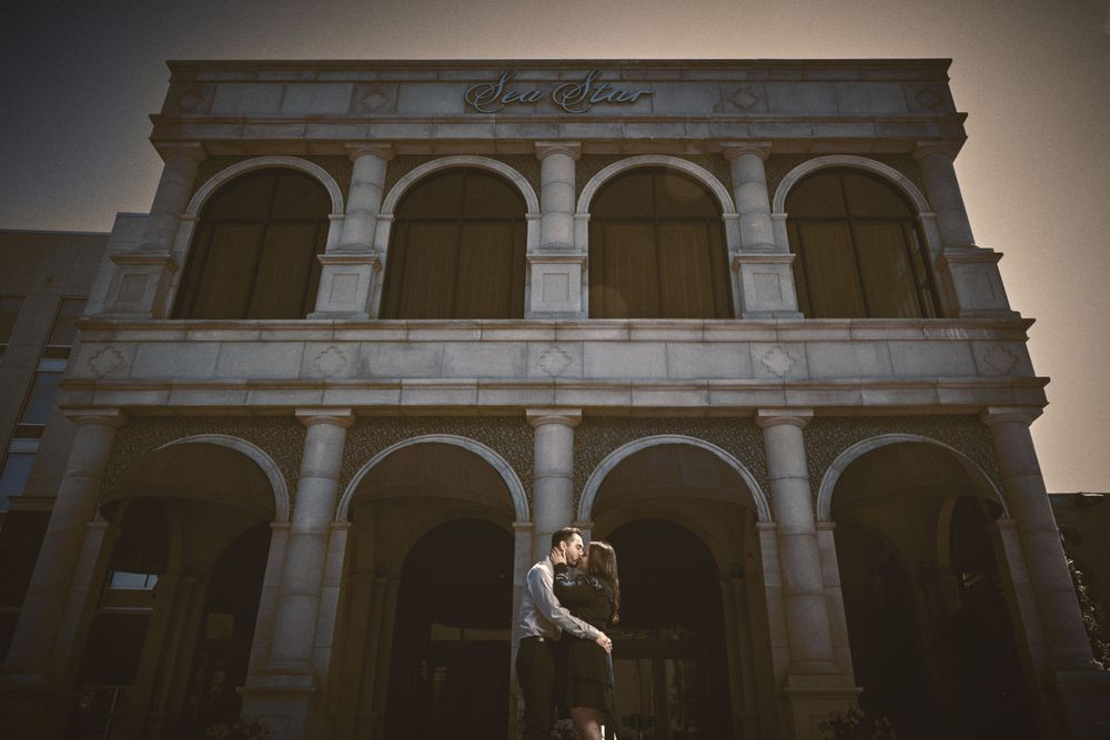A couple embraces in front of a classical stone archway building at sunset.