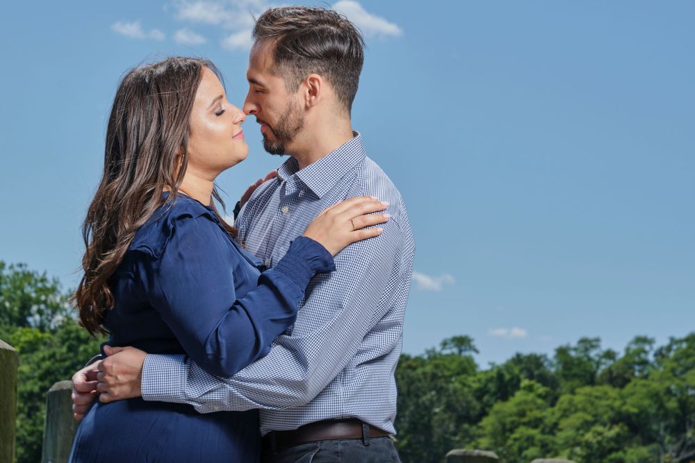 A couple shares an intimate moment against a backdrop of green trees and blue sky.
