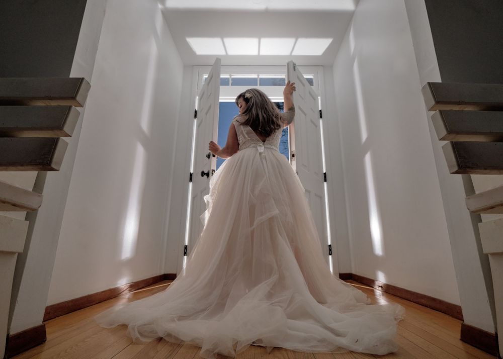 A bride in a flowing white gown walks down a bright modern hallway.