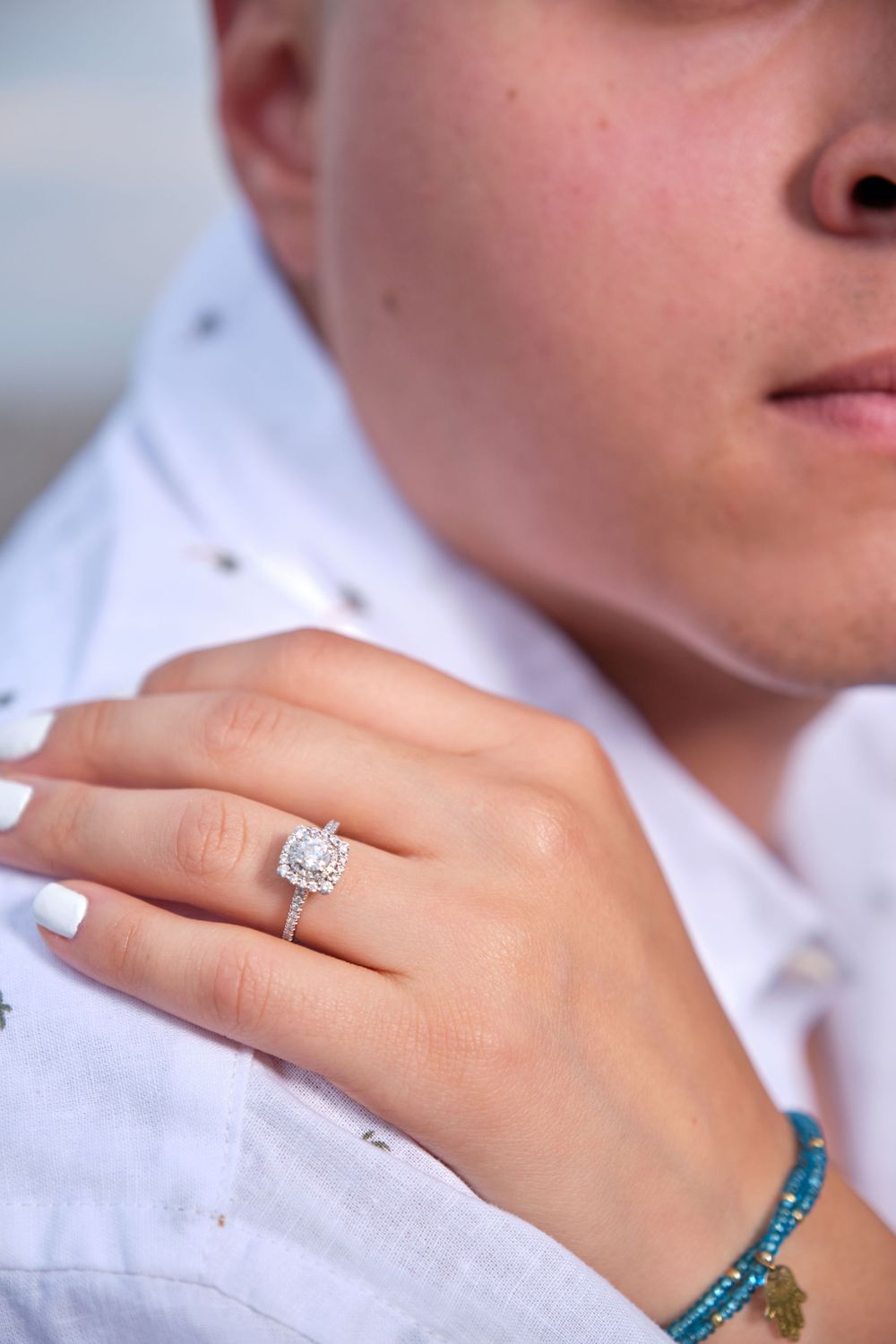 Close up of a sparkling diamond engagement ring on someone's hand with turquoise bracelet.