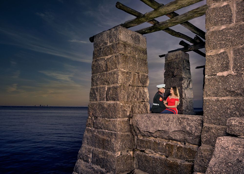 Couple in red against stone architecture overlooking dramatic seaside sunset view.