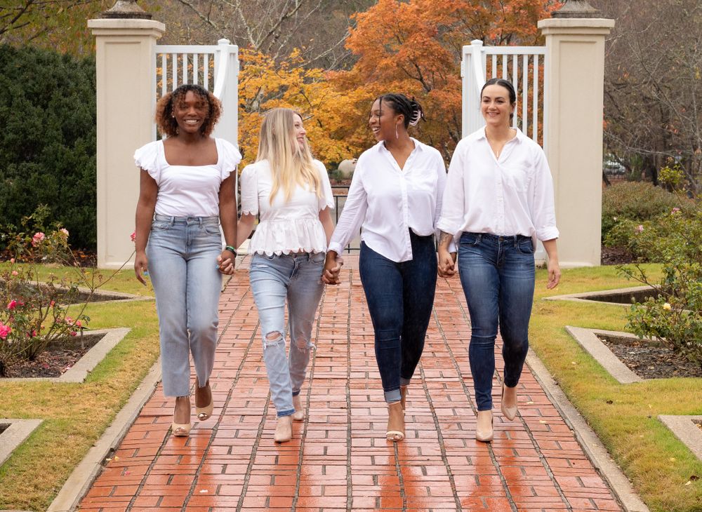 Four friends walking together on a brick pathway during autumn.