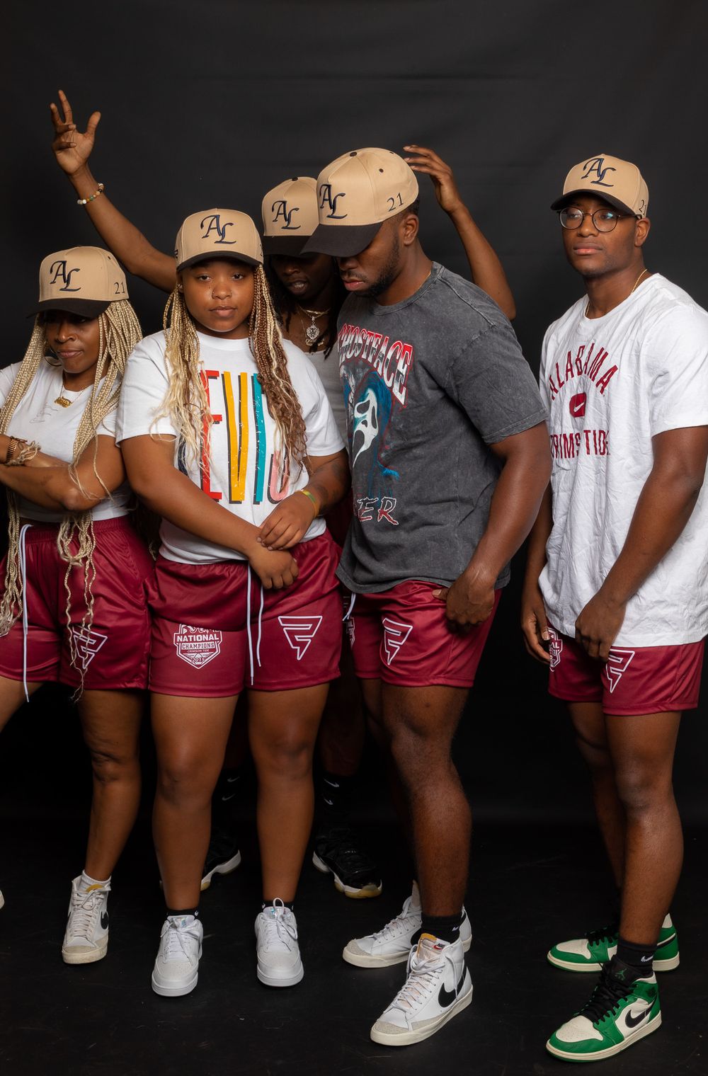 Group wearing matching burgundy shorts and baseball caps posing against black background.