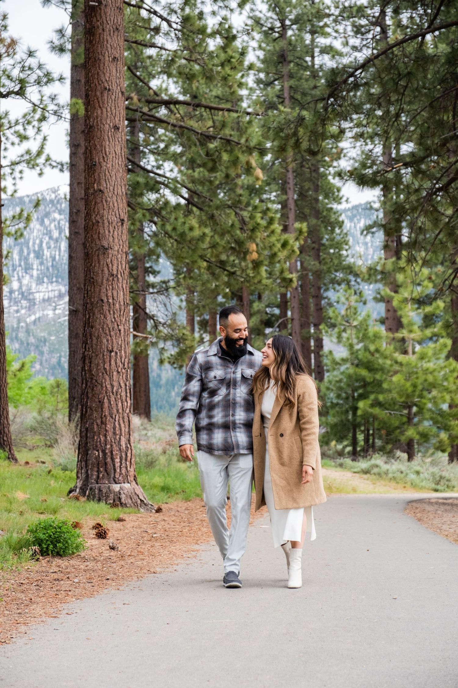 Two people strolling together on a paved path through a scenic pine forest on a mountain trail.