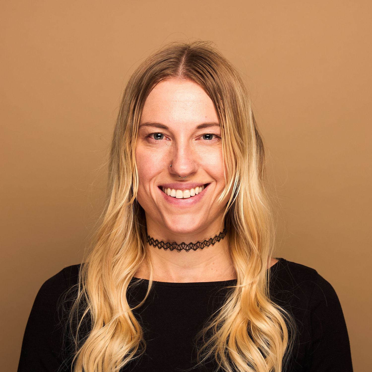 Professional portrait of person with long blonde hair wearing black top and choker necklace.