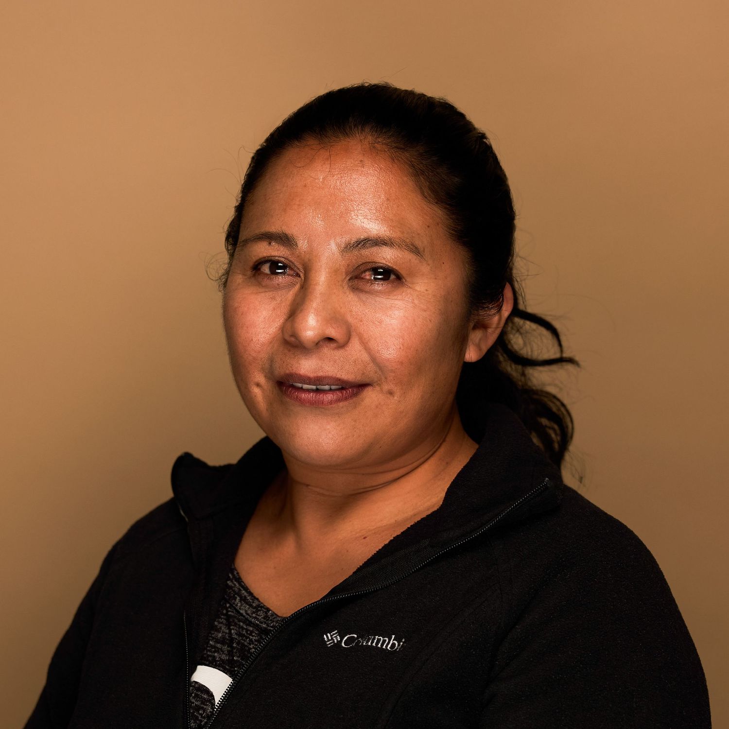 Portrait of person in black Columbia jacket against warm brown background.