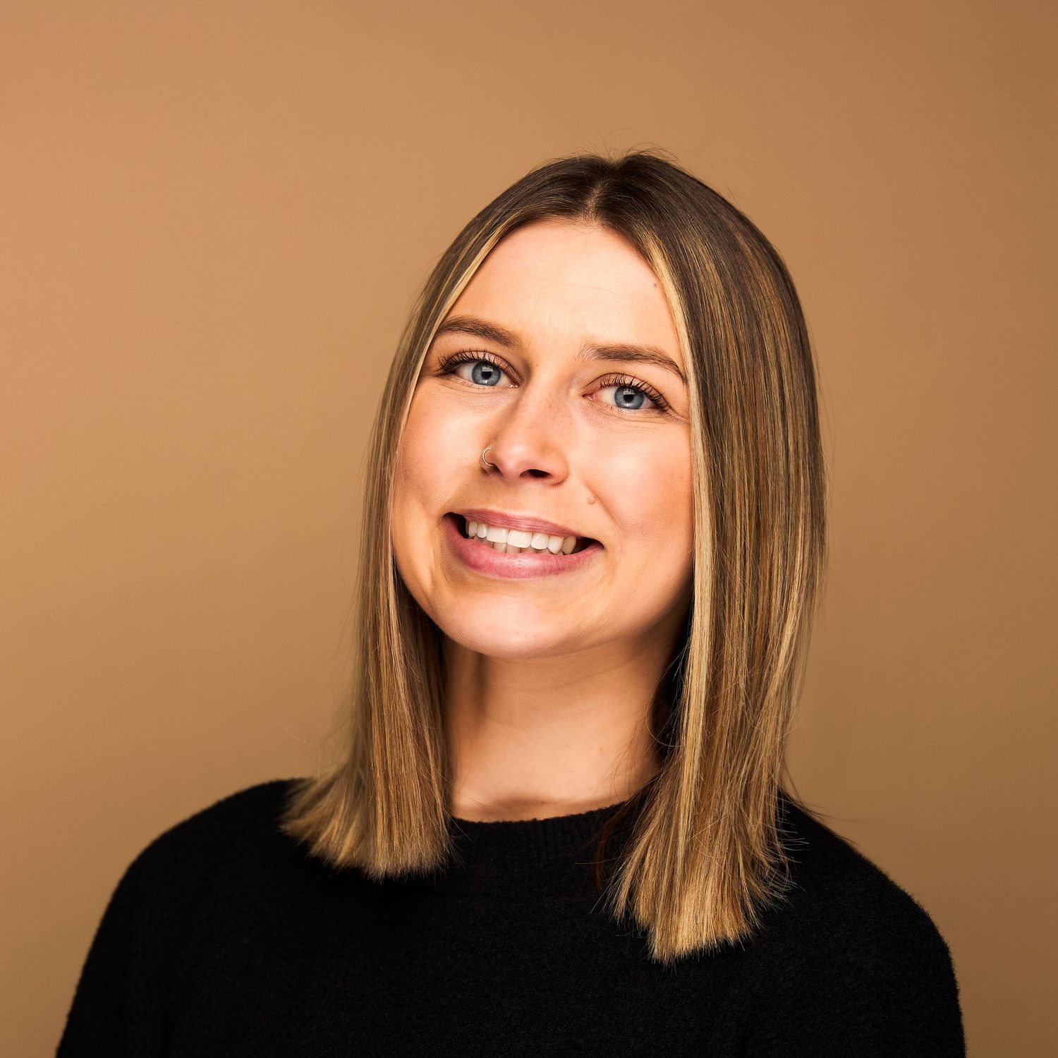 Professional headshot of person with shoulder-length blonde hair wearing black sweater.