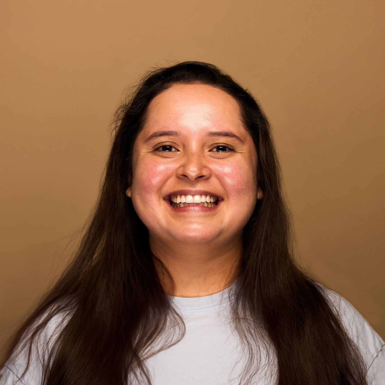 Portrait of person with long dark hair wearing white t-shirt against brown background.