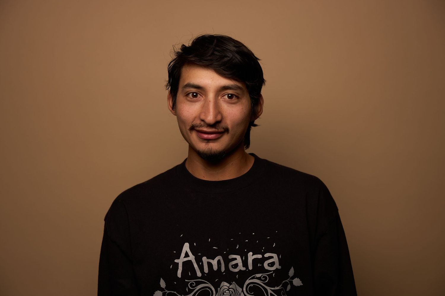 Portrait of a smiling man wearing a black Amara t-shirt against brown background.