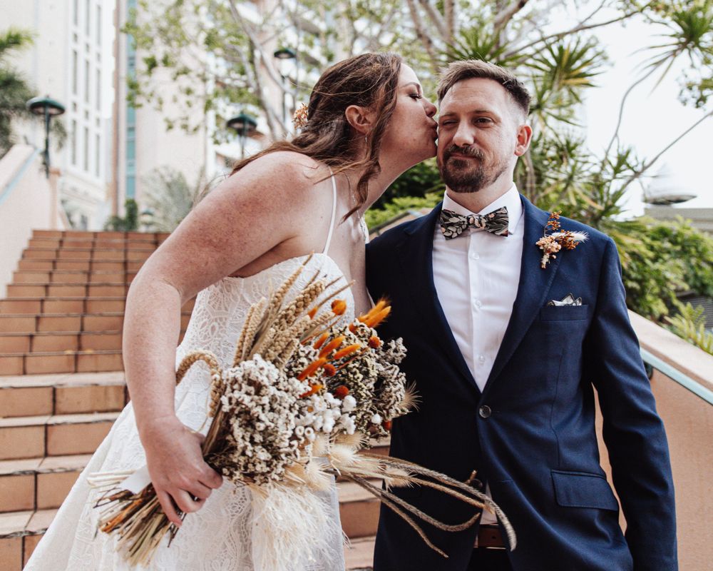 Romantic wedding couple shares intimate moment on outdoor staircase with dried floral bouquet.