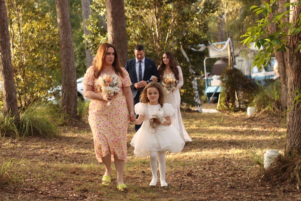 An intimate outdoor wedding ceremony taking place among tall trees with decorative white fabric draping.