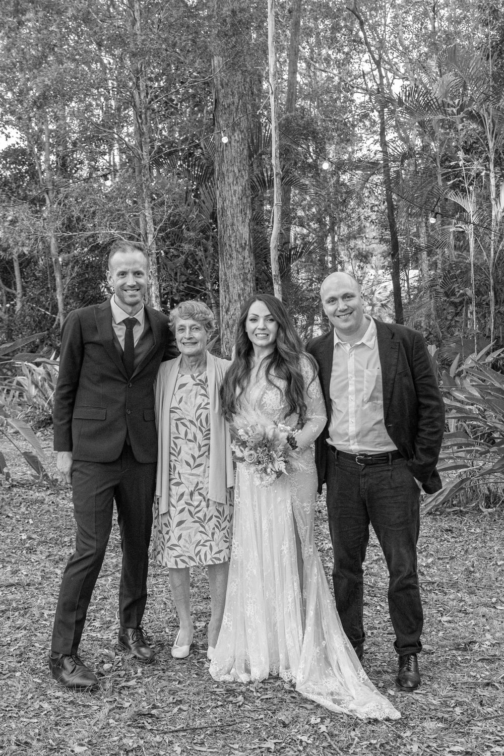 Black and white portrait of small wedding group standing together in wooded setting.