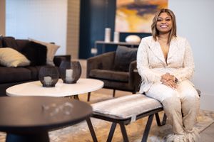 Business woman in white outfit sitting relaxed in modern living room setting.