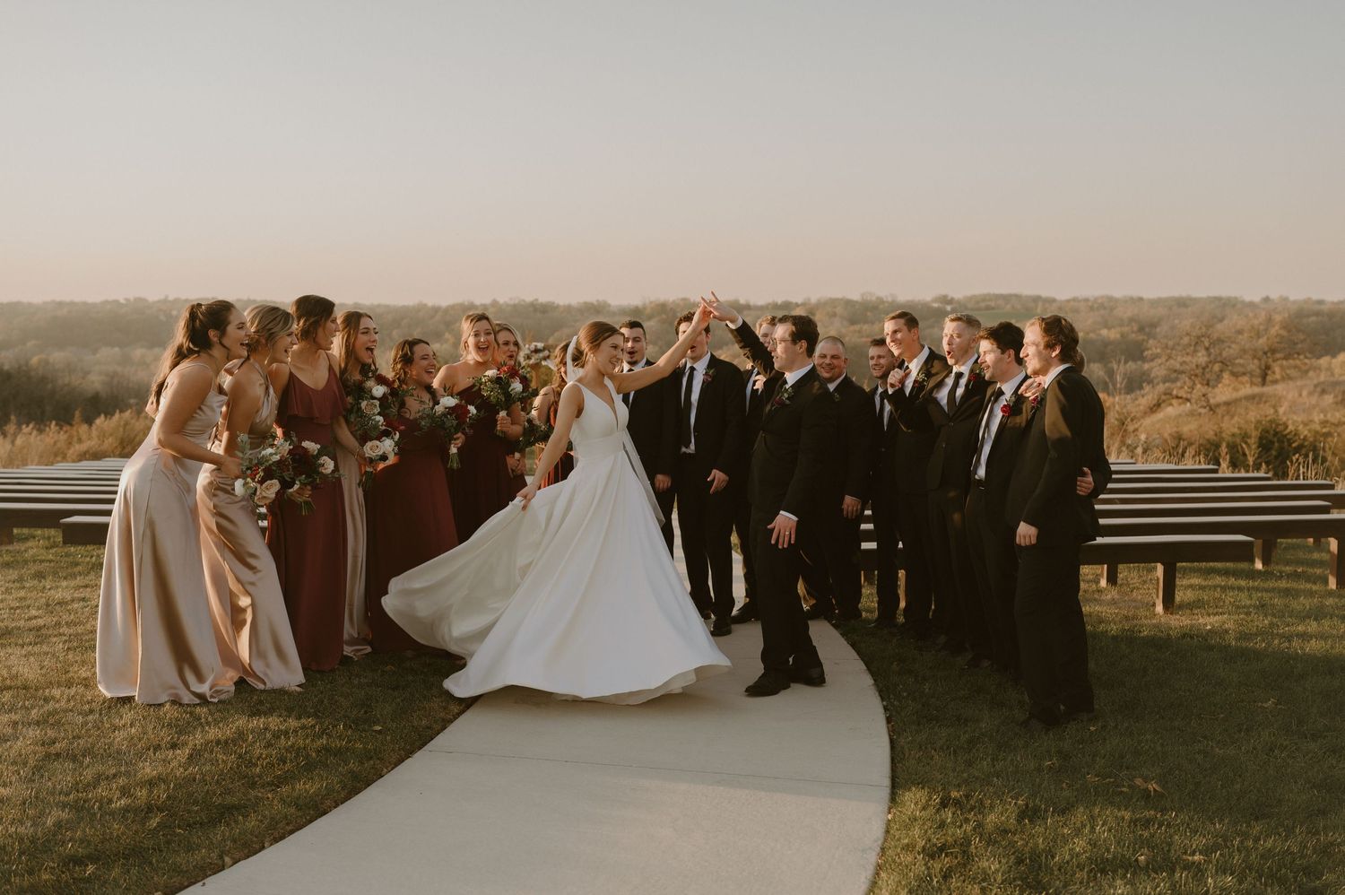Wedding party celebrates on outdoor path with scenic autumn backdrop.