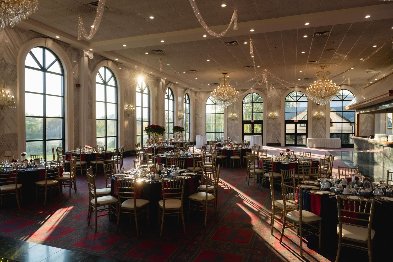 Elegant ballroom with arched windows, crystal chandeliers, and round tables set for a formal event.