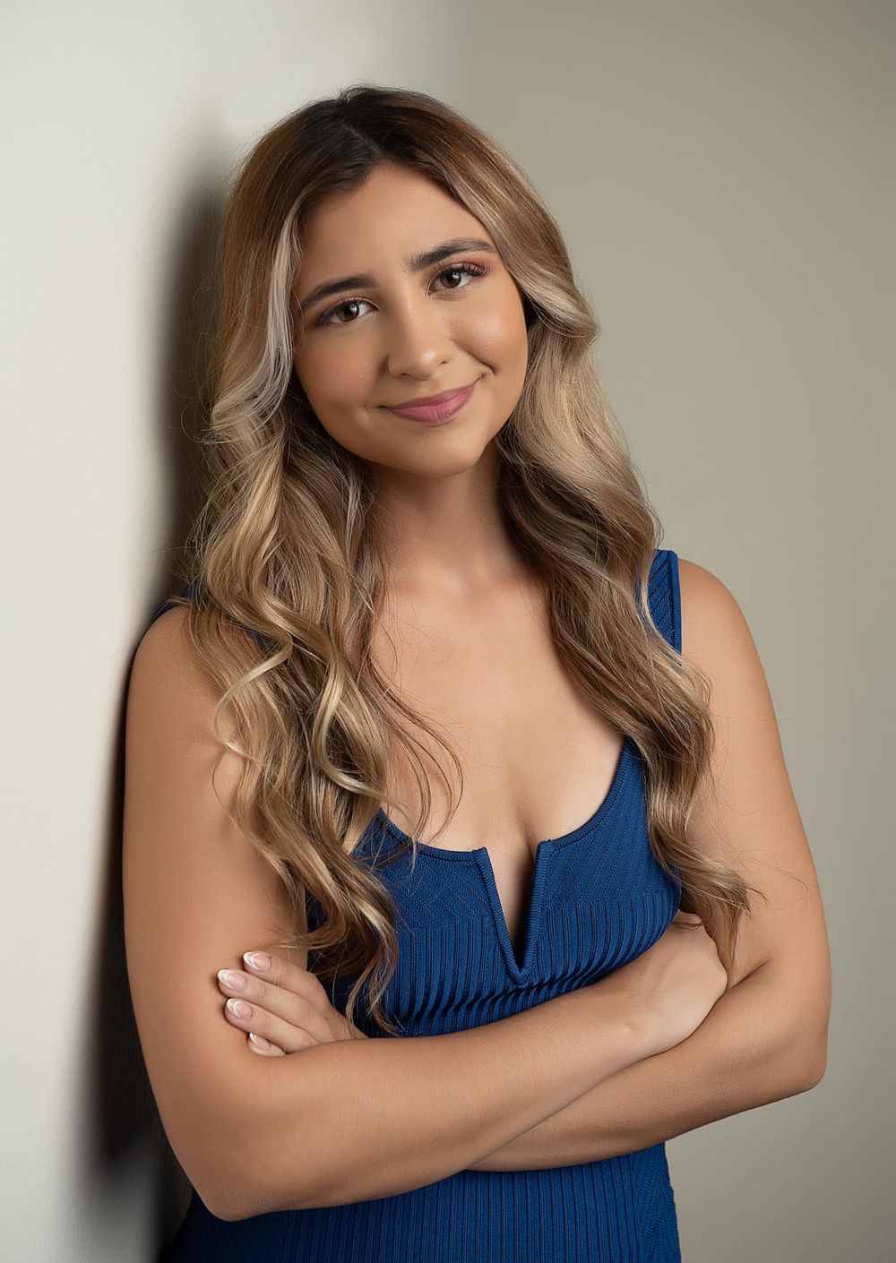 Studio portrait of a person with long wavy hair wearing a blue sleeveless dress.