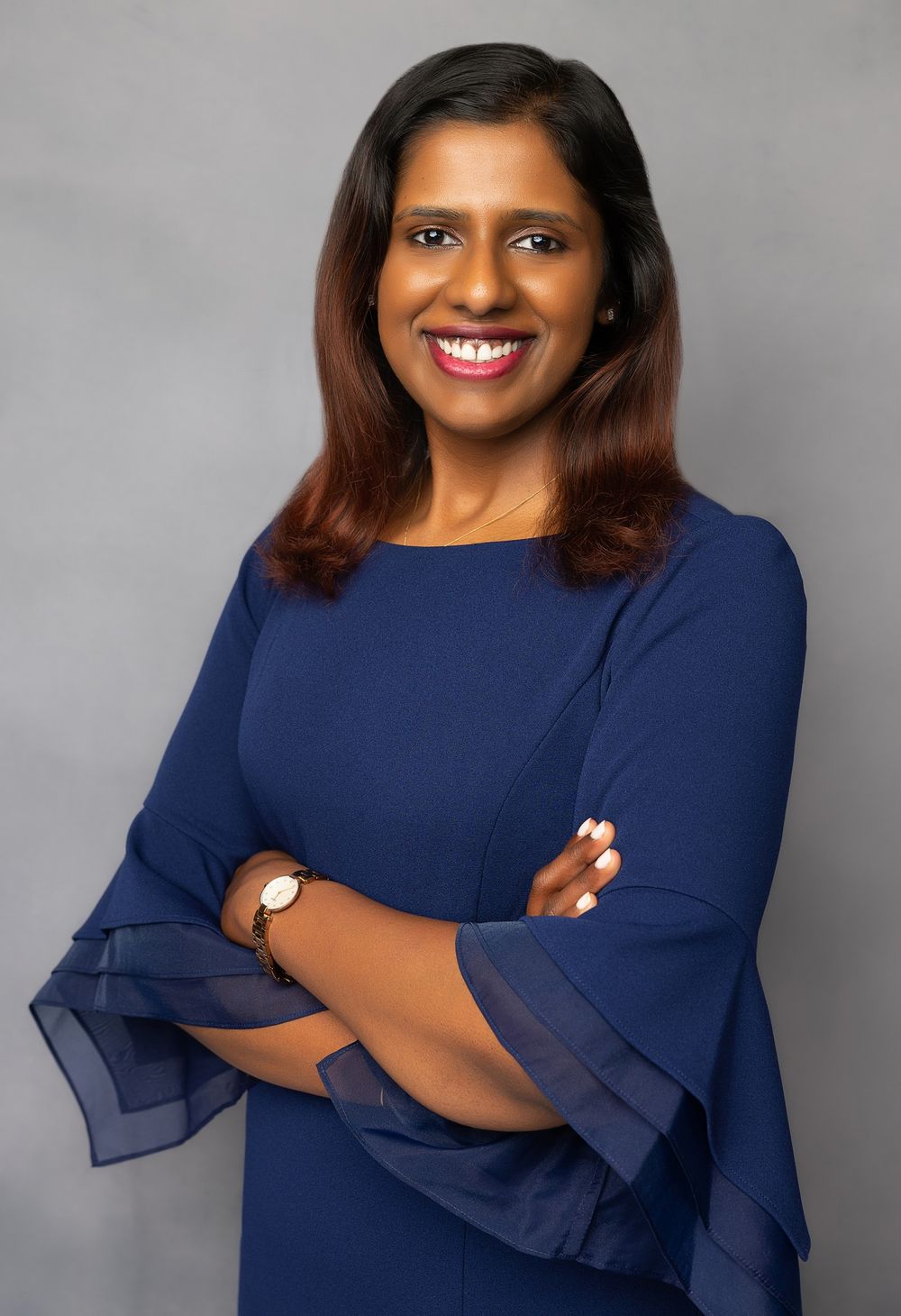Business portrait of woman in navy dress with bell sleeves against gray background.