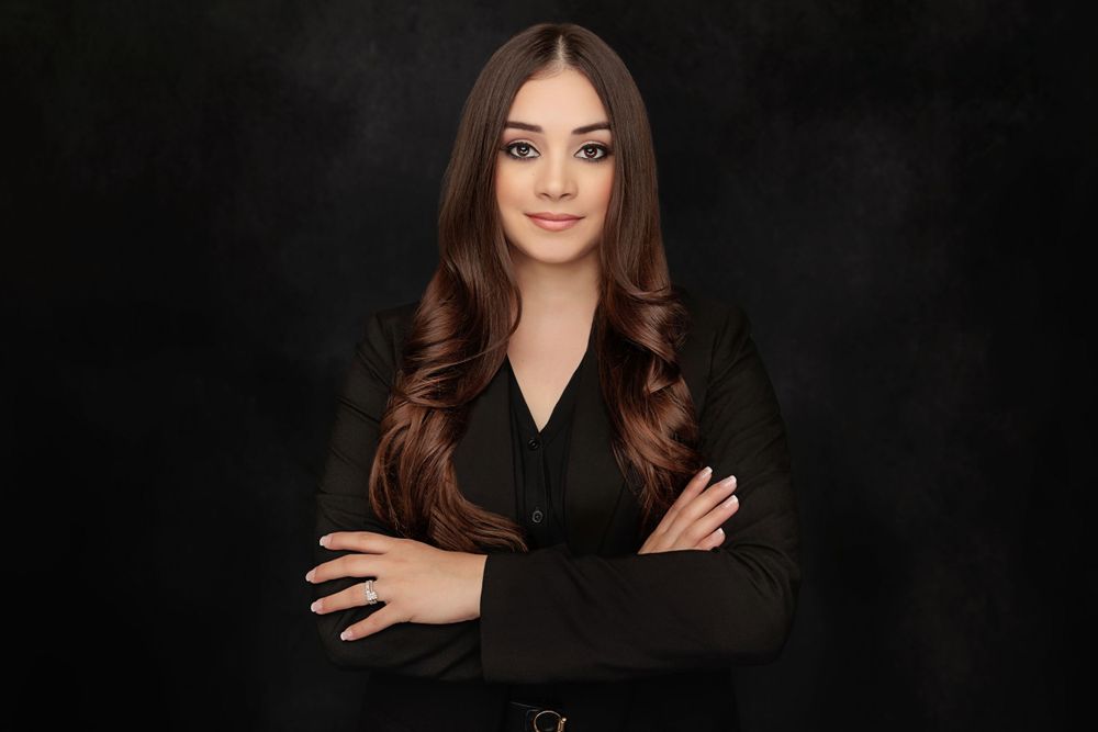 Professional portrait of woman in black blazer against dark background.