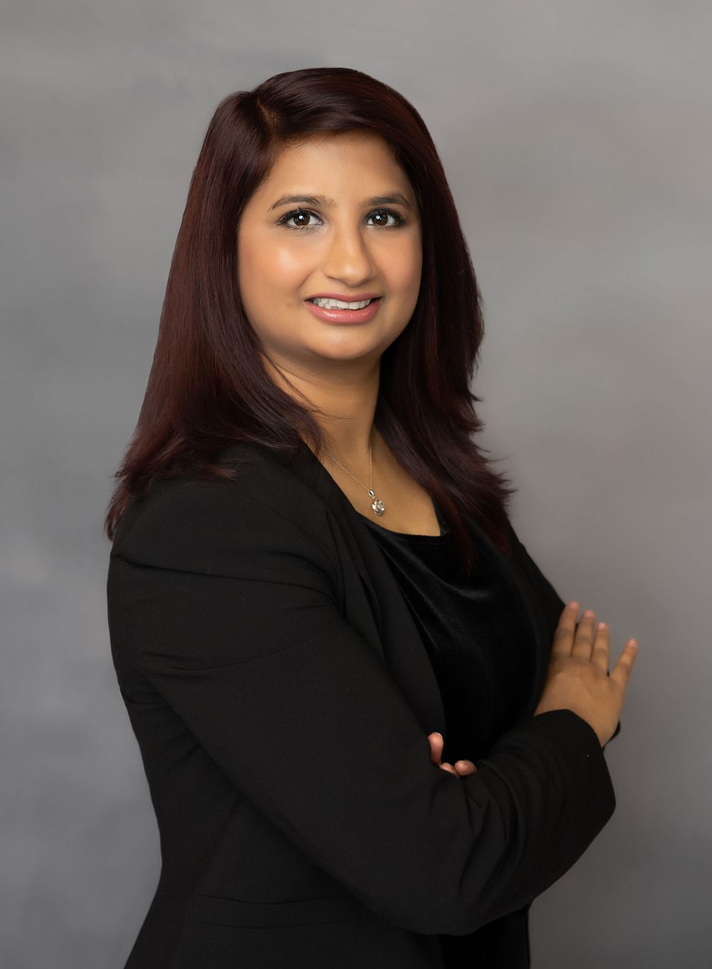 Professional corporate headshot in black blazer against neutral backdrop.