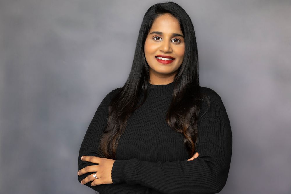 Professional portrait of a woman in black sweater with long dark hair against grey background.