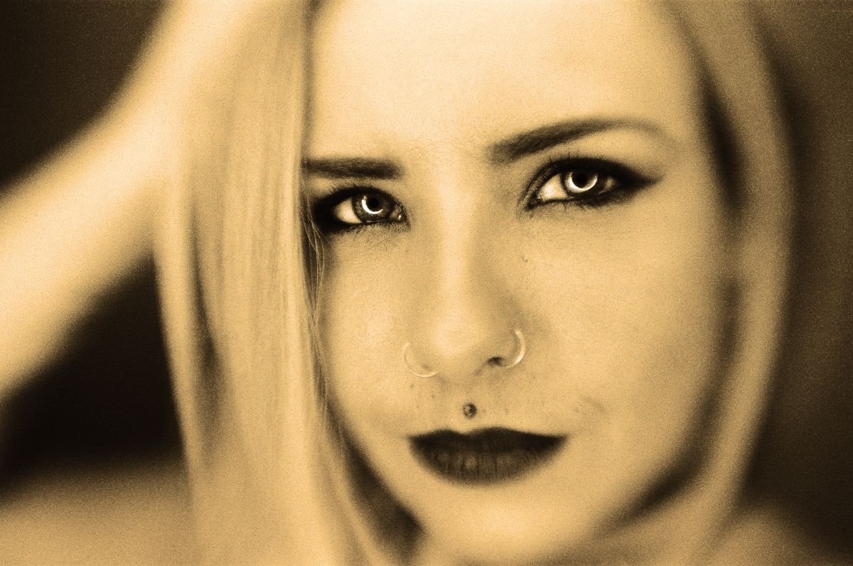 Sepia-toned close-up portrait with striking eyes and dark lipstick.