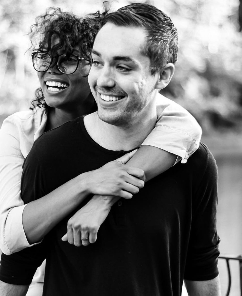 Black and white photo of joyful interracial couple embracing and laughing outdoors.